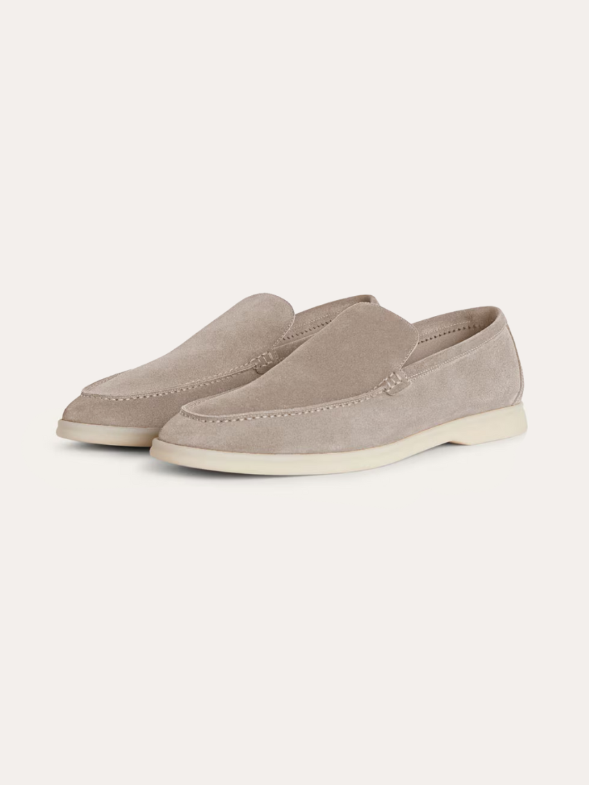 Ein Paar beigefarbene Wildleder-Loafer für Herren mit einer weißen Kontrastsohle, schräg von der Seite fotografiert auf einem weißen Hintergrund.  