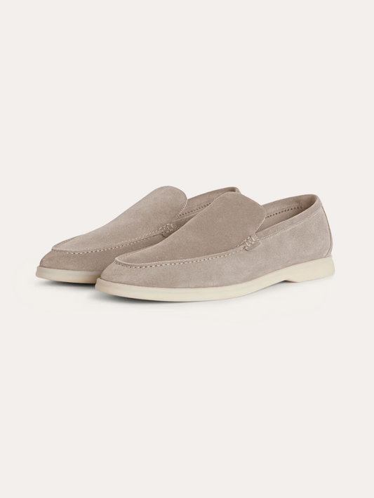Ein Paar beigefarbene Wildleder-Loafer für Herren mit einer weißen Kontrastsohle, schräg von der Seite fotografiert auf einem weißen Hintergrund.  
